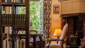 A library with bookshelves, a reading chair, a fireplace, and a view of greenery through a window. - Hôtel La Casa Païral (Collioure)