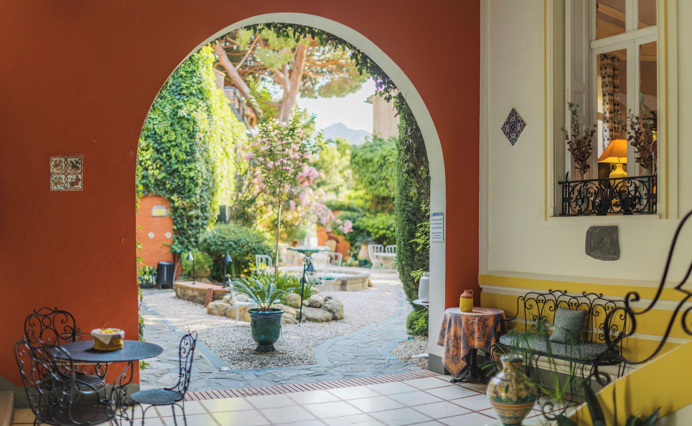 An outdoor patio area with a tiled floor, a table with chairs, a potted plant, and a decorative wall with a window.