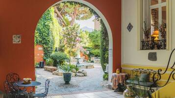 An outdoor patio area with a tiled floor, a table with chairs, a potted plant, and a decorative wall with a window.