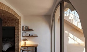 A room with a brick fireplace, bookshelves, a desk with a lamp, and a large window overlooking a staircase. - Hôtel La Casa Païral (Collioure)