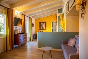 A room with a wooden floor, a sofa, a small round table, a dresser, and a mirror. - Hôtel La Casa Païral (Collioure)