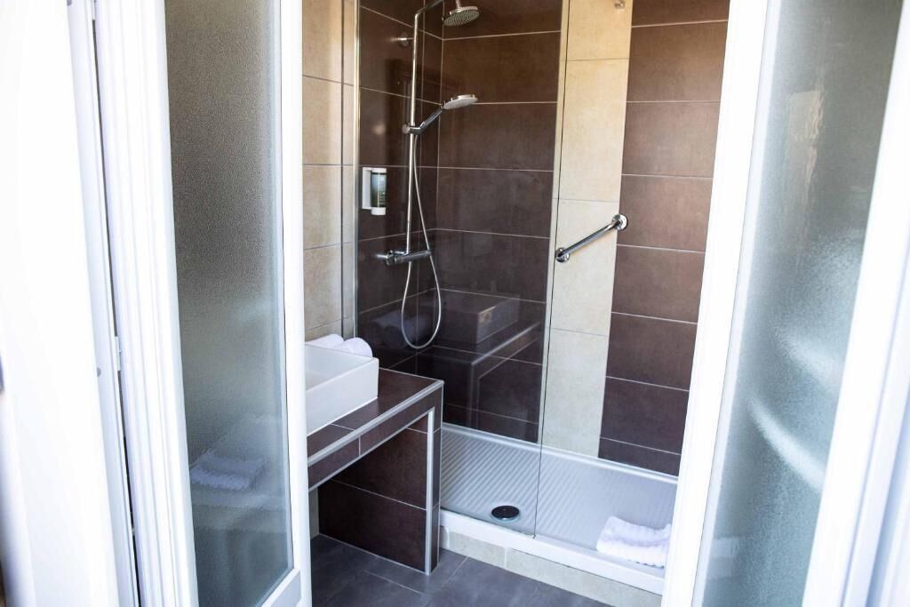 A shower with a glass door, a white sink, and a small bench.
