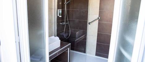 A shower with a glass door, a white sink, and a small bench.