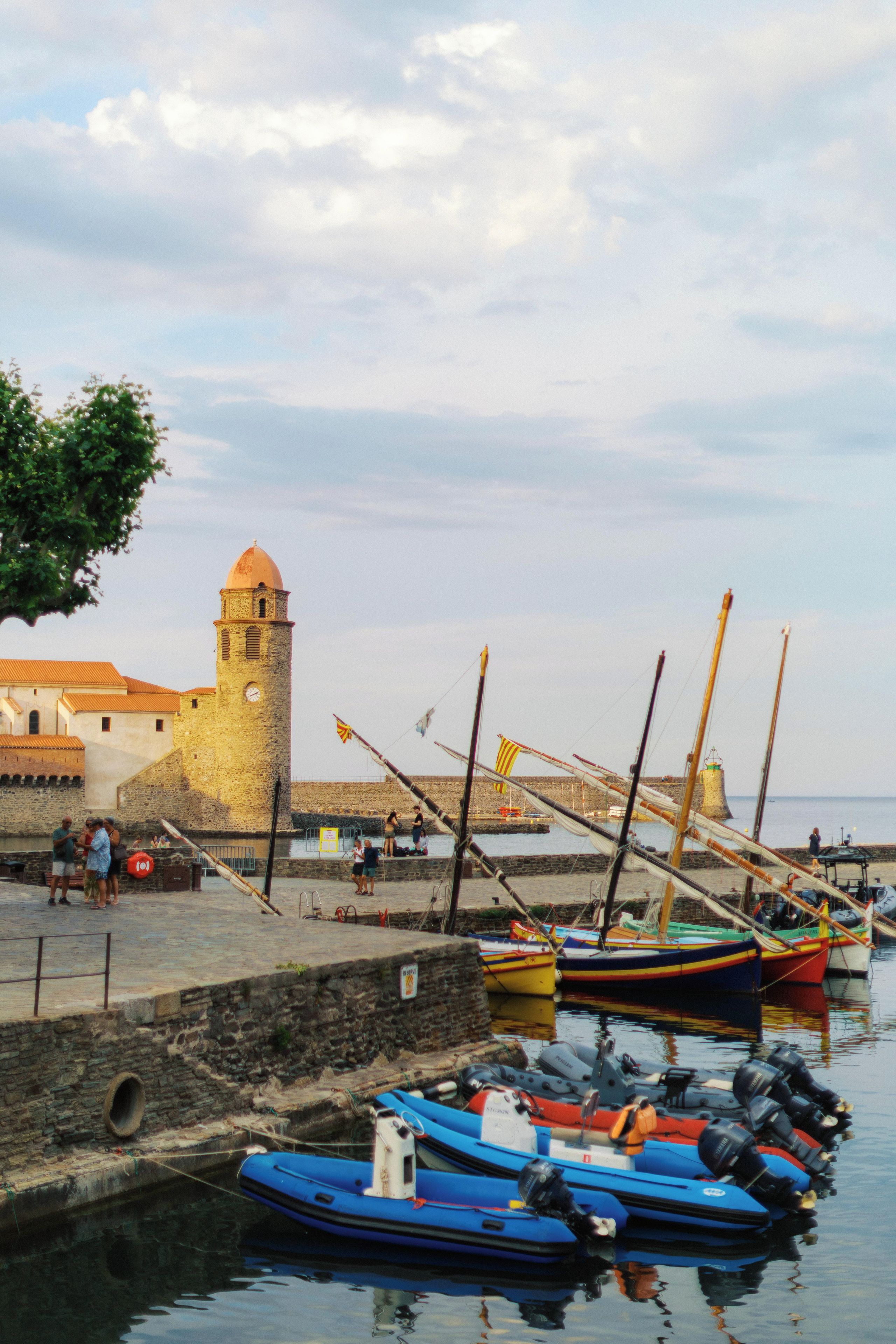 A harbor with boats, a lighthouse, and a stone building with a tower.