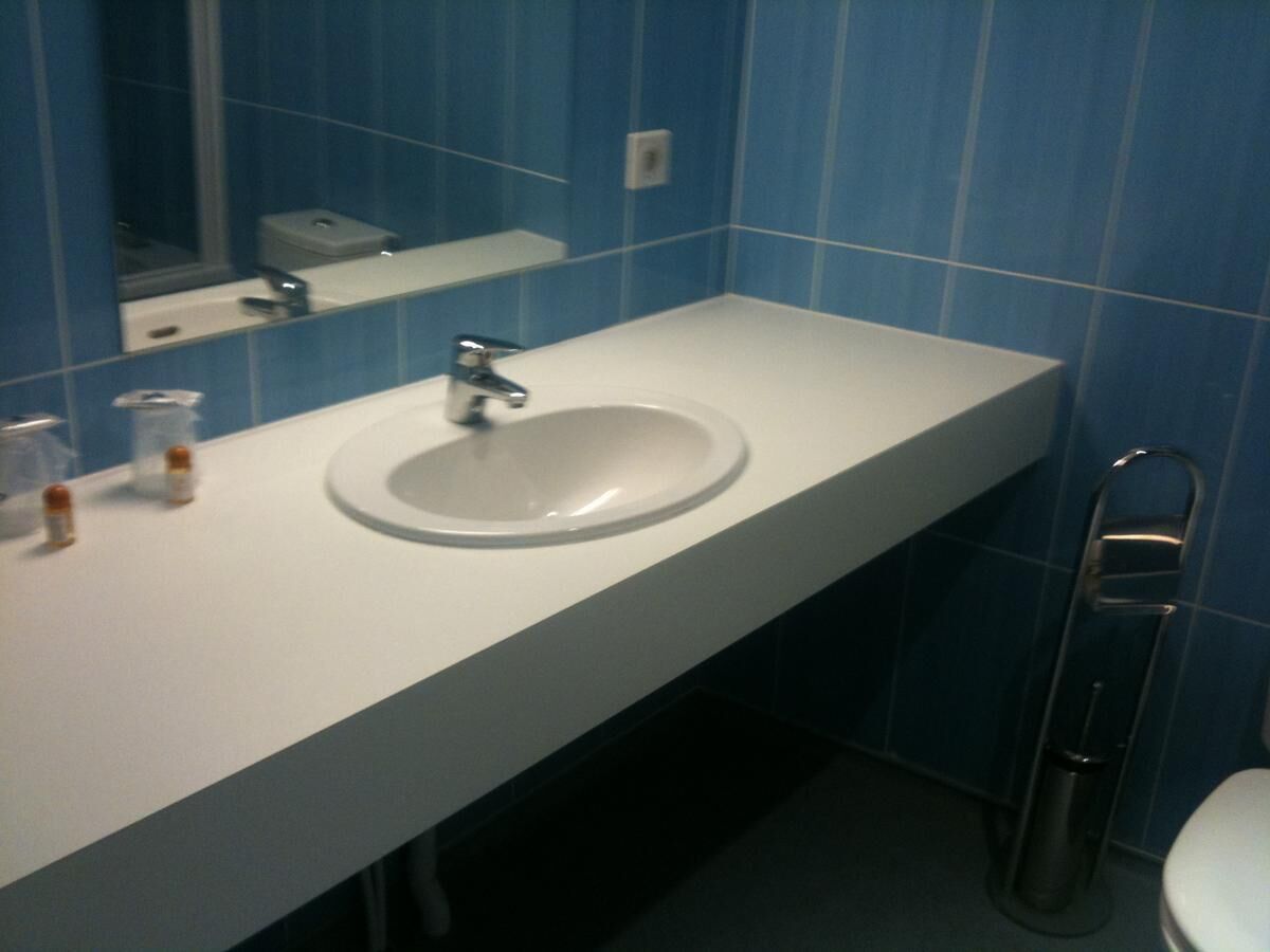 A bathroom with a white sink, blue-tiled walls, a mirror, and a toilet.
