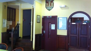 A hallway with a staircase, a door with a sign, and a coat rack. - Croix de Malte (Lourdes)