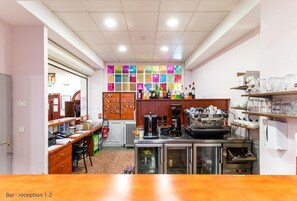 A bar area with a reception desk, shelves with bottles, a coffee machine, and a refrigerator. - Croix de Malte (Lourdes)