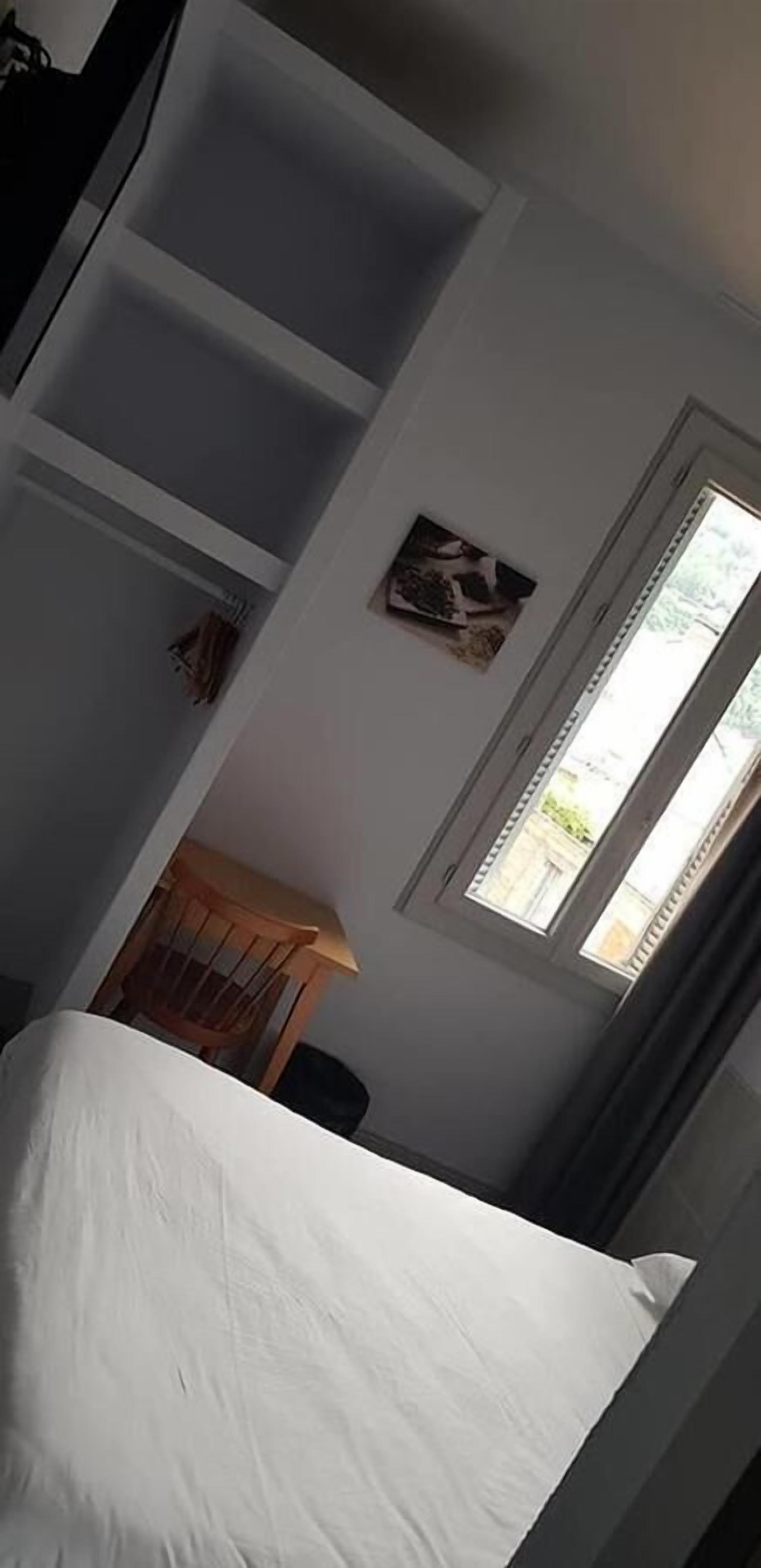 A bedroom with a bed, a wooden chair, a small table, and a window with curtains.
