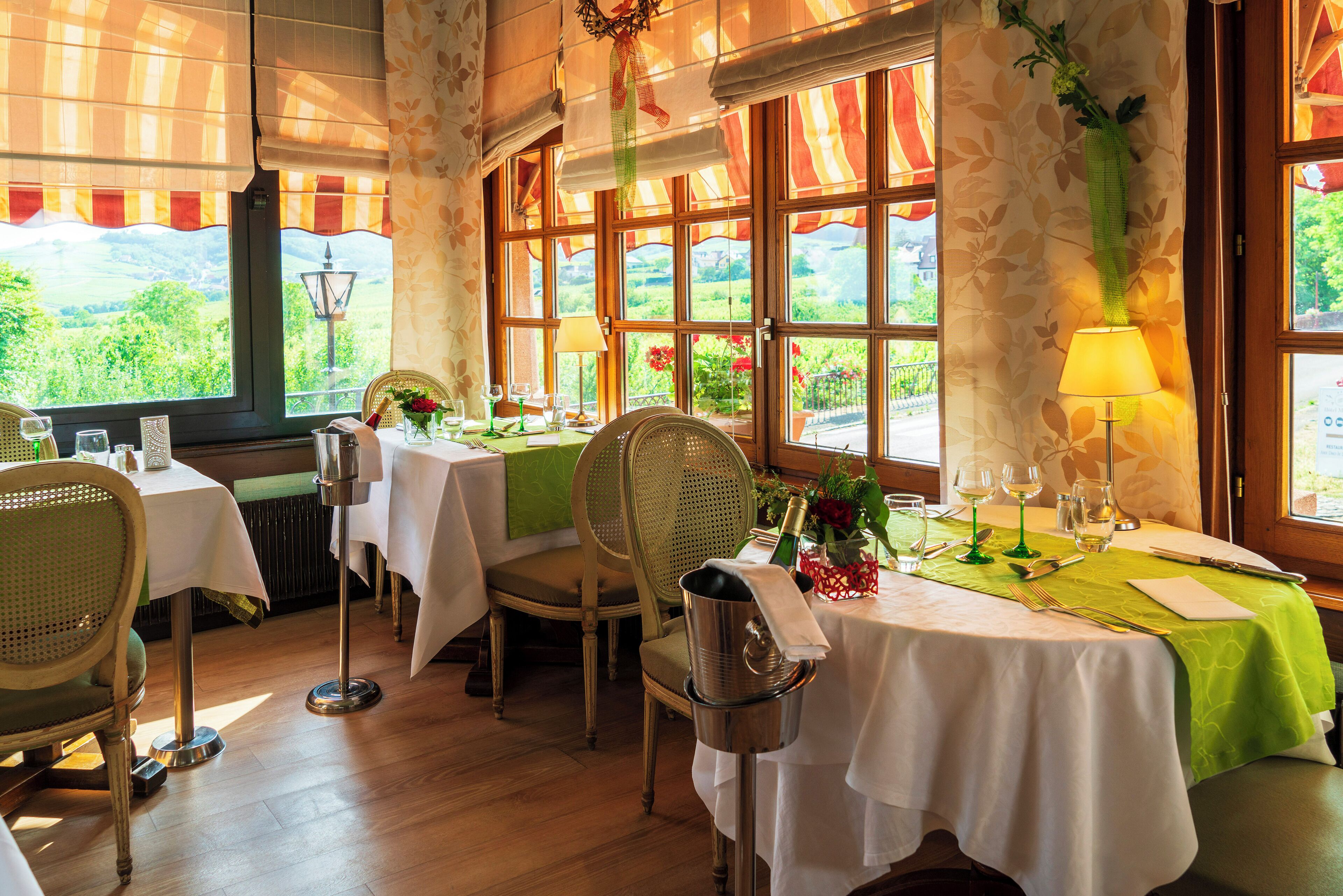 A dining area with tables set for two, featuring white tablecloths and green accents.