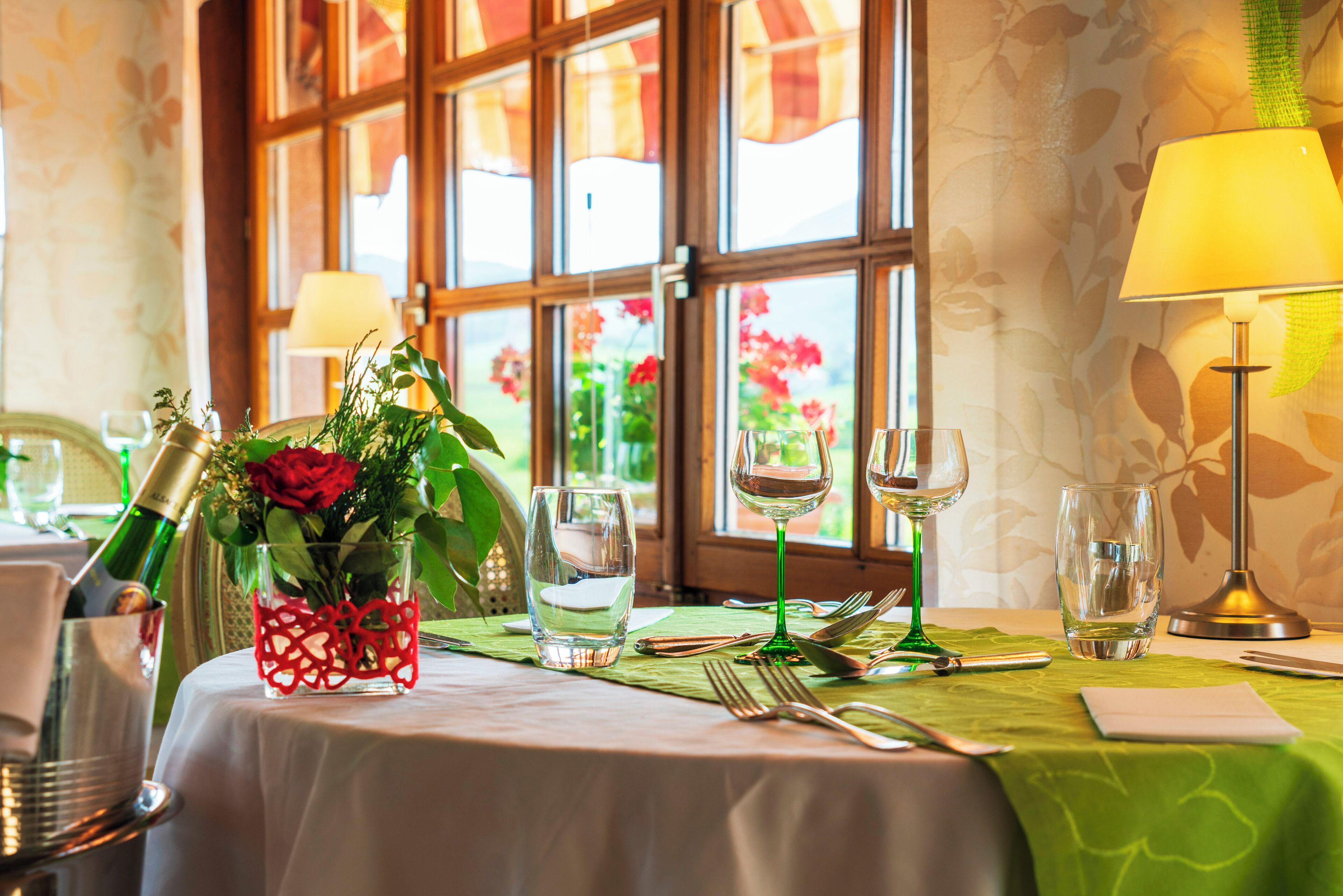 A dining table set with a bottle of champagne, a vase of flowers, and various glassware.