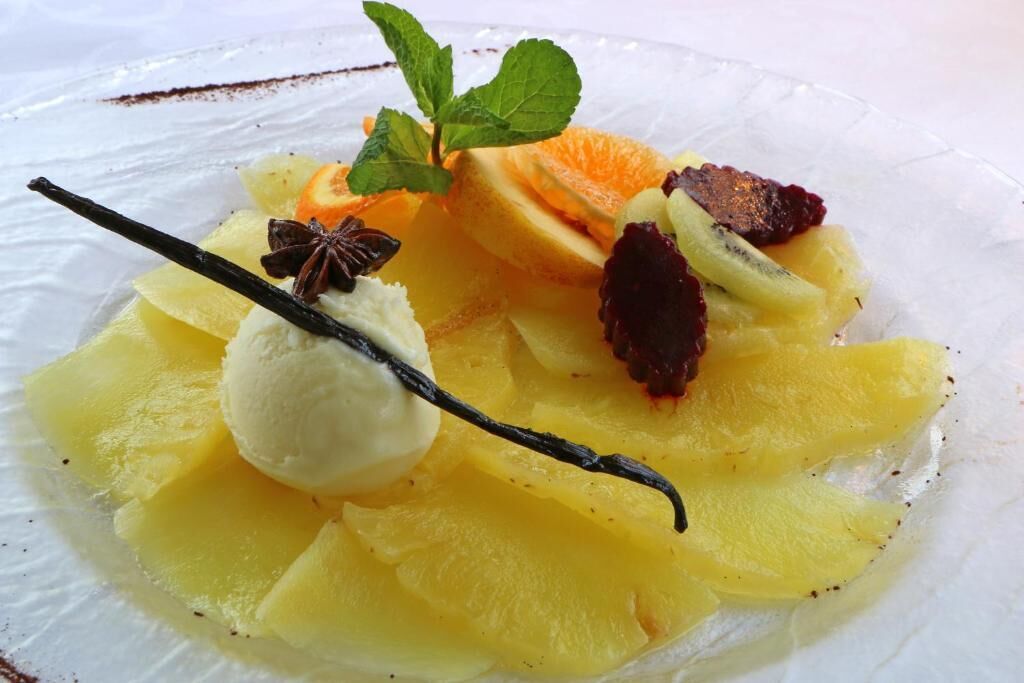 A dessert plate with sliced fruits and a vanilla scoop.