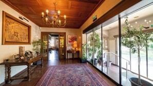 A lobby with a wooden ceiling, a chandelier, a large rug, and potted plants.
