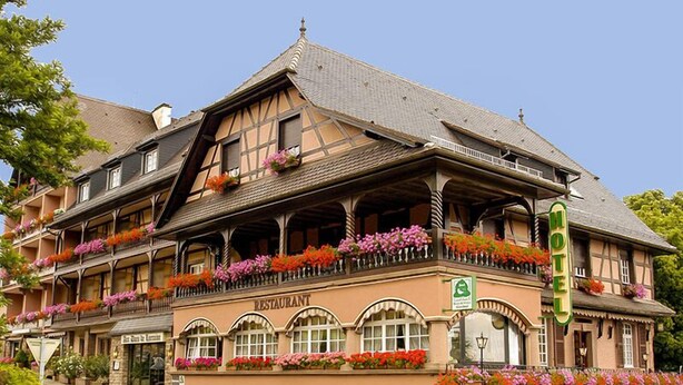 A traditional European hotel with a restaurant on the ground floor, multiple balconies with flower boxes, and a sign indicating it is a hotel.