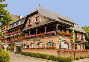 A traditional European hotel with a restaurant on the ground floor, multiple balconies with flower boxes, and a sign indicating it is a hotel.