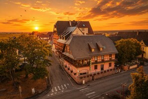 A hotel with a traditional European architectural style, featuring a prominent gabled roof and a balcony with red awnings.