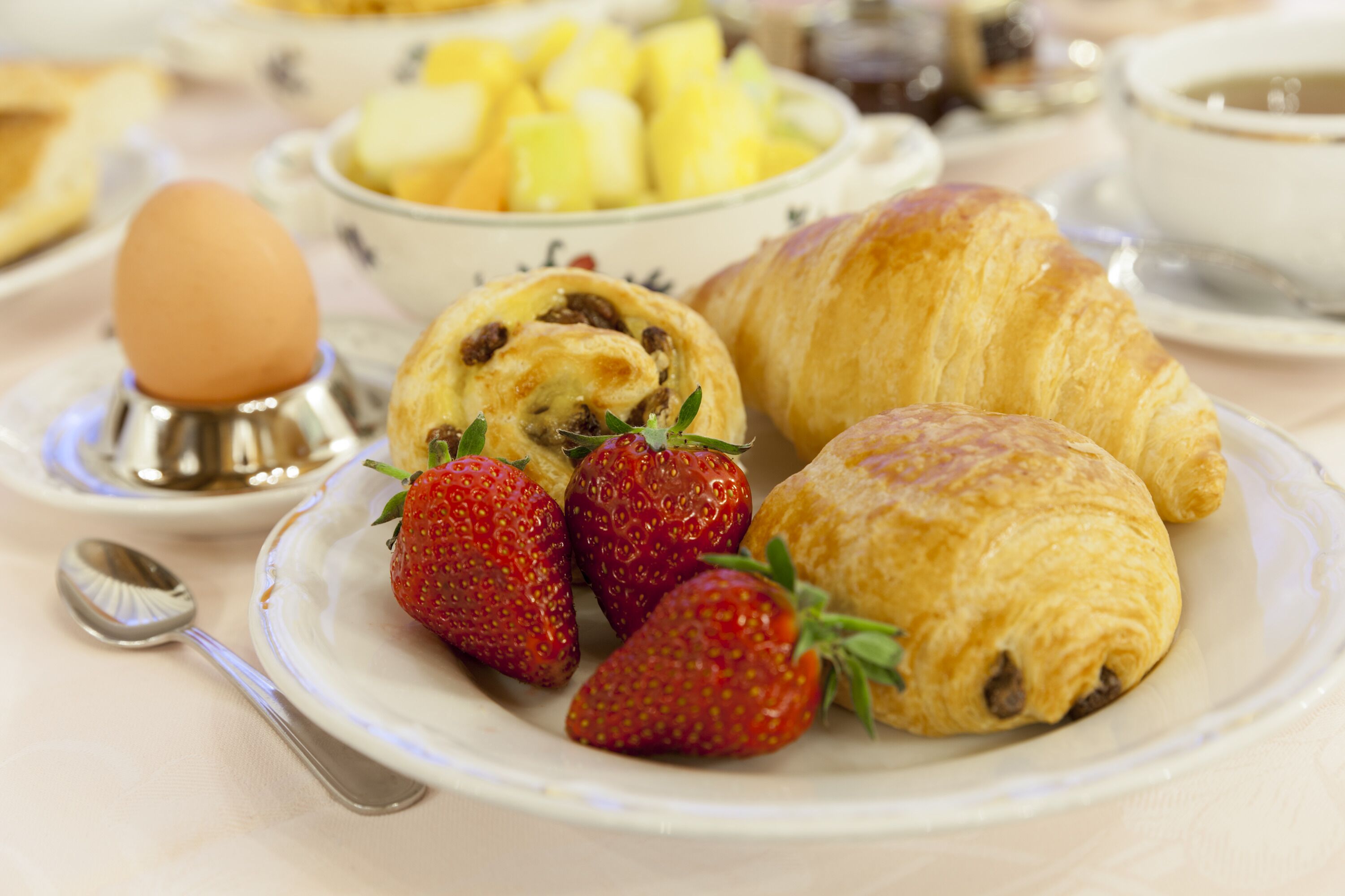 Un desayuno con croissants, fresas y un bol de fruta.