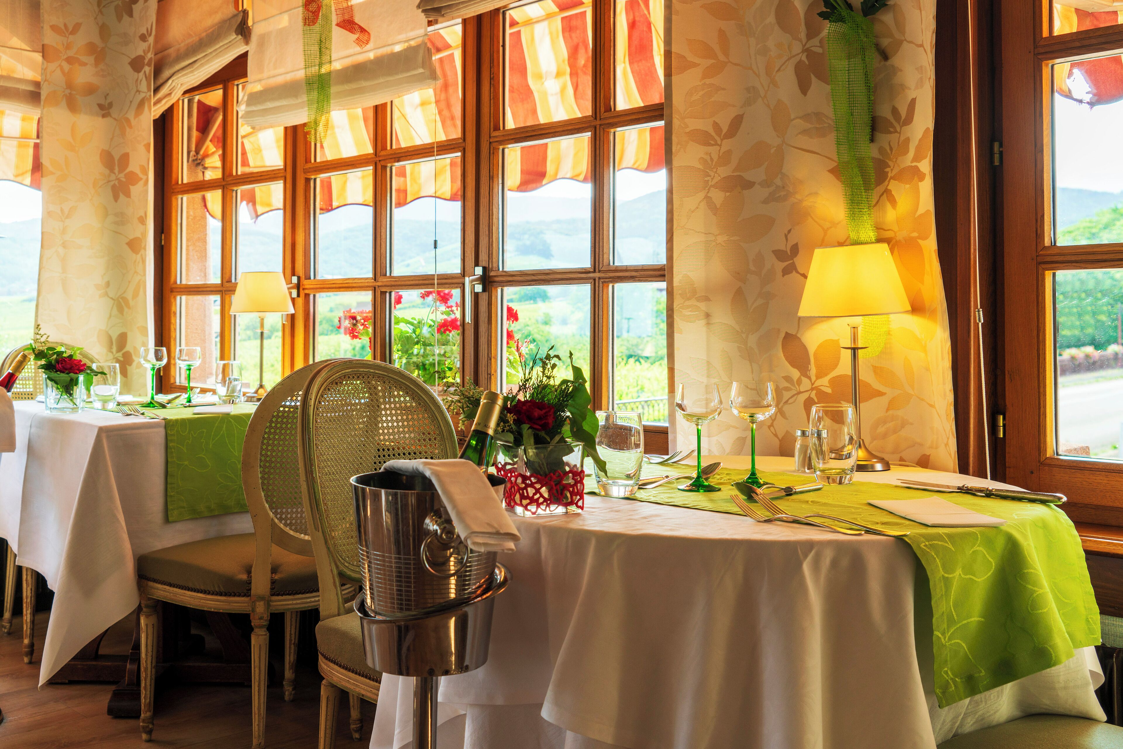 Uma sala de jantar com mesas preparadas para dois, com vista para o exterior através de grandes janelas.