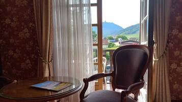 A room with a view of a green landscape through sheer curtains.