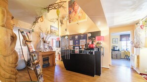 A spacious room with a wooden floor, a reception desk, a large statue, and various decorations including a map and framed pictures. - Hostellerie du Château (Eguisheim)