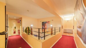 A hotel corridor with a red carpet, a railing, and a painting on the wall. - Hostellerie du Château (Eguisheim)