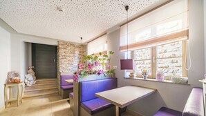 A modern interior with a stone accent wall, a purple cushioned bench, a wooden table, and a window with blinds. - Hostellerie du Château (Eguisheim)