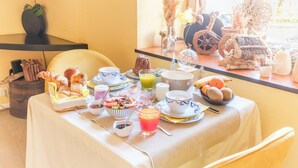 A breakfast table with various food items and drinks, a chair, and a window with a view of the outside. - Hostellerie du Château (Eguisheim)