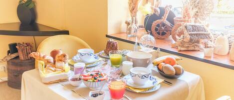 A breakfast table with various food items and drinks, a chair, and a window with a view of the outside.