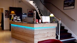 A reception desk with a wooden finish and blue LED lighting, a staircase with a black railing, and a framed poster on the wall. - Les Charmilles (Lux)