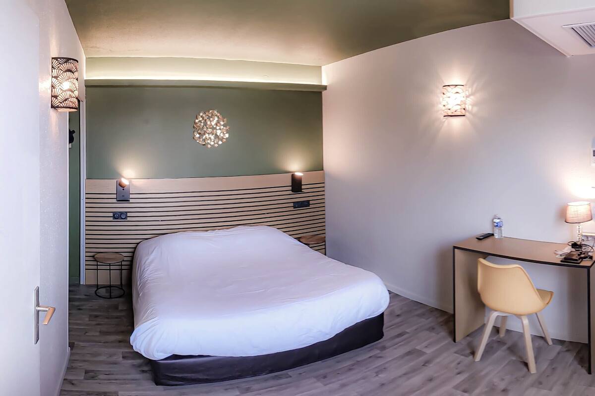 Une chambre d’hôtel comprenant un lit, un bureau avec une chaise, une lampe et un luminaire fixé au mur.
