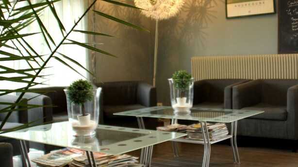 A modern reception area with glass tables, a large potted plant, and a wall-mounted light fixture. - Les Charmilles (Lux)