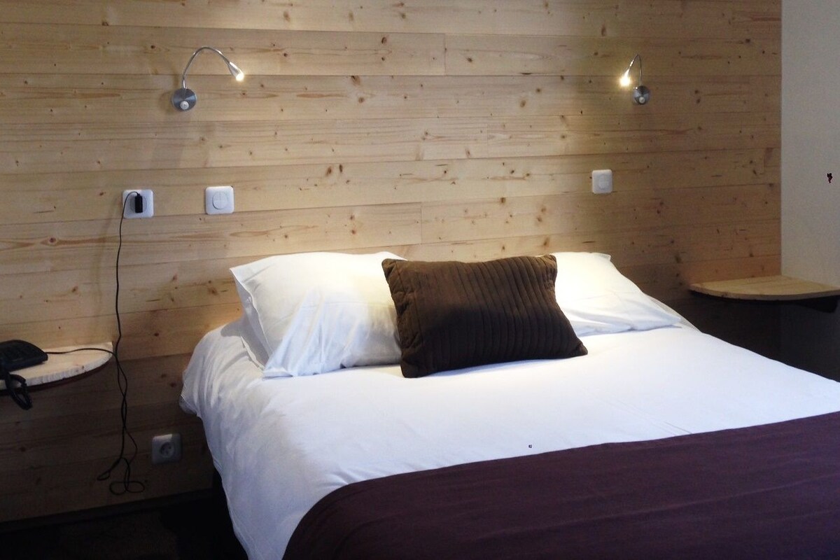 A hotel room with a wooden headboard, a bed with white linens, a brown throw pillow, bedside tables with lamps, and a phone on one table.