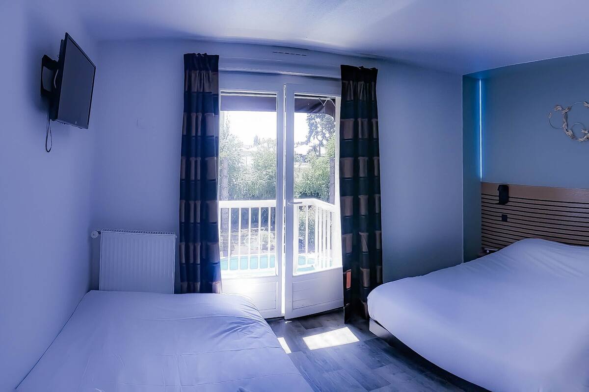 Une chambre d’hôtel avec deux lits, une télévision, une porte-fenêtre coulissante donnant sur un balcon et un luminaire fixé au mur.