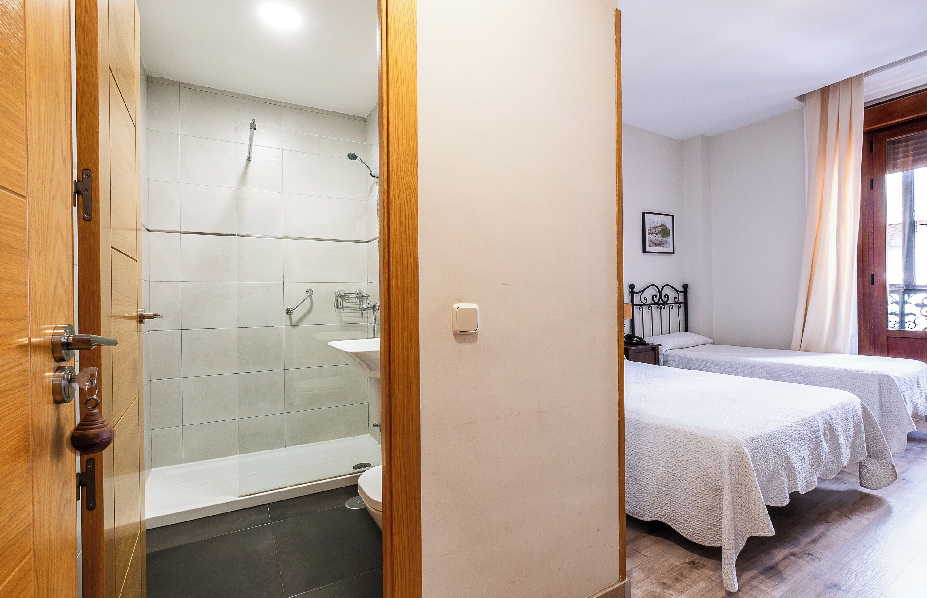 A hotel room with a shower, a sink, and two beds.