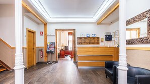 A hotel lobby with a reception desk, wooden paneling, a fire extinguisher, and a wall-mounted information board. - Hostal El Pilar (Madrid)