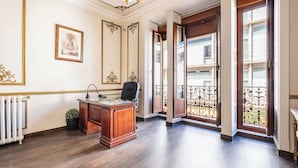 A spacious office with a wooden desk, a chair, and a radiator. There are framed pictures on the wall and a balcony with a wrought iron railing. - Hostal El Pilar (Madrid)