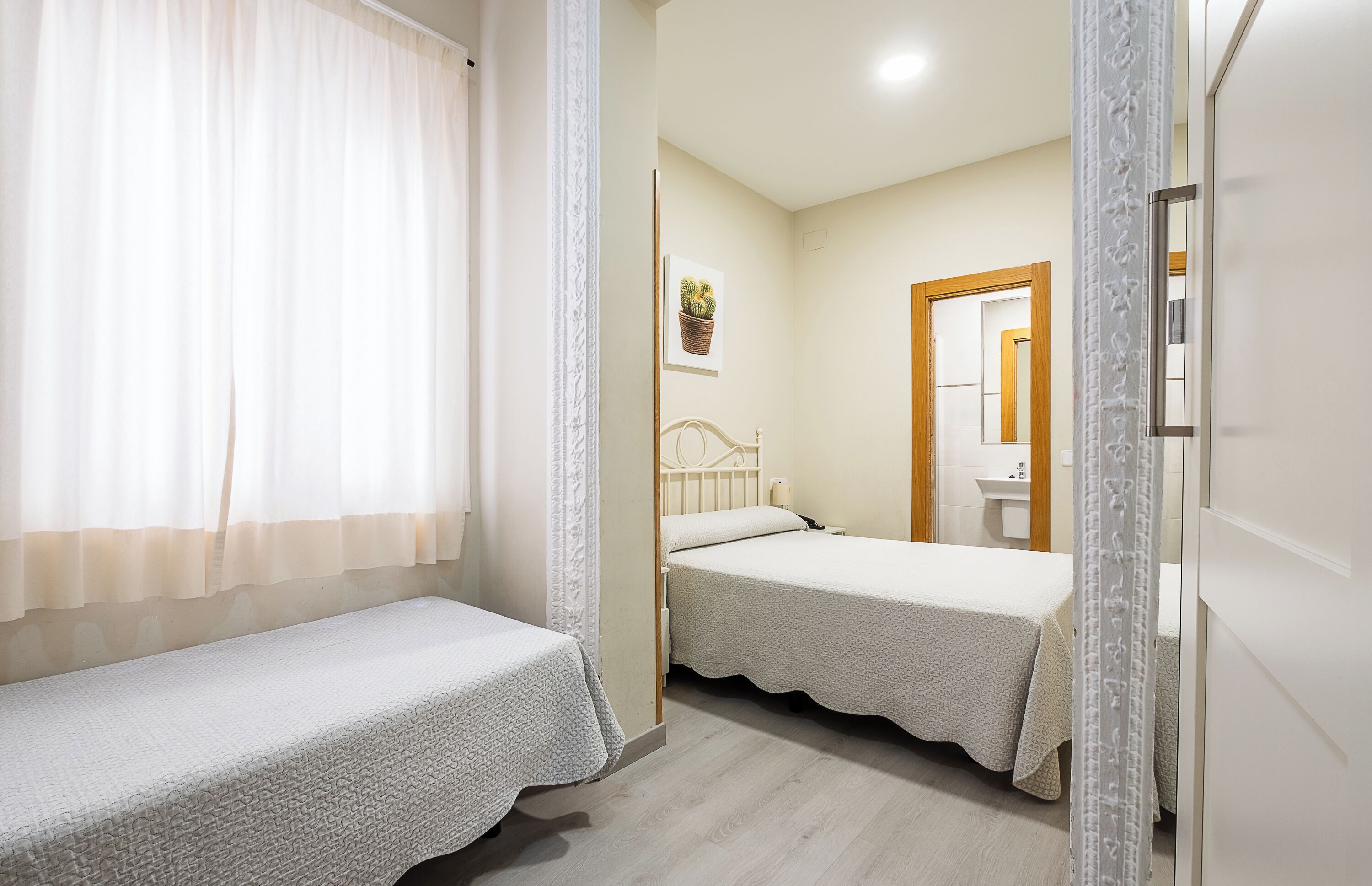 Un dormitorio con dos camas individuales, una mesita de noche con lámpara, un cuadro en la pared y una puerta que da al baño.