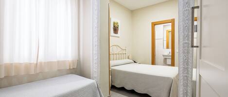 A bedroom with two single beds, a bedside table with a lamp, a wall-mounted picture, and a door leading to a bathroom.