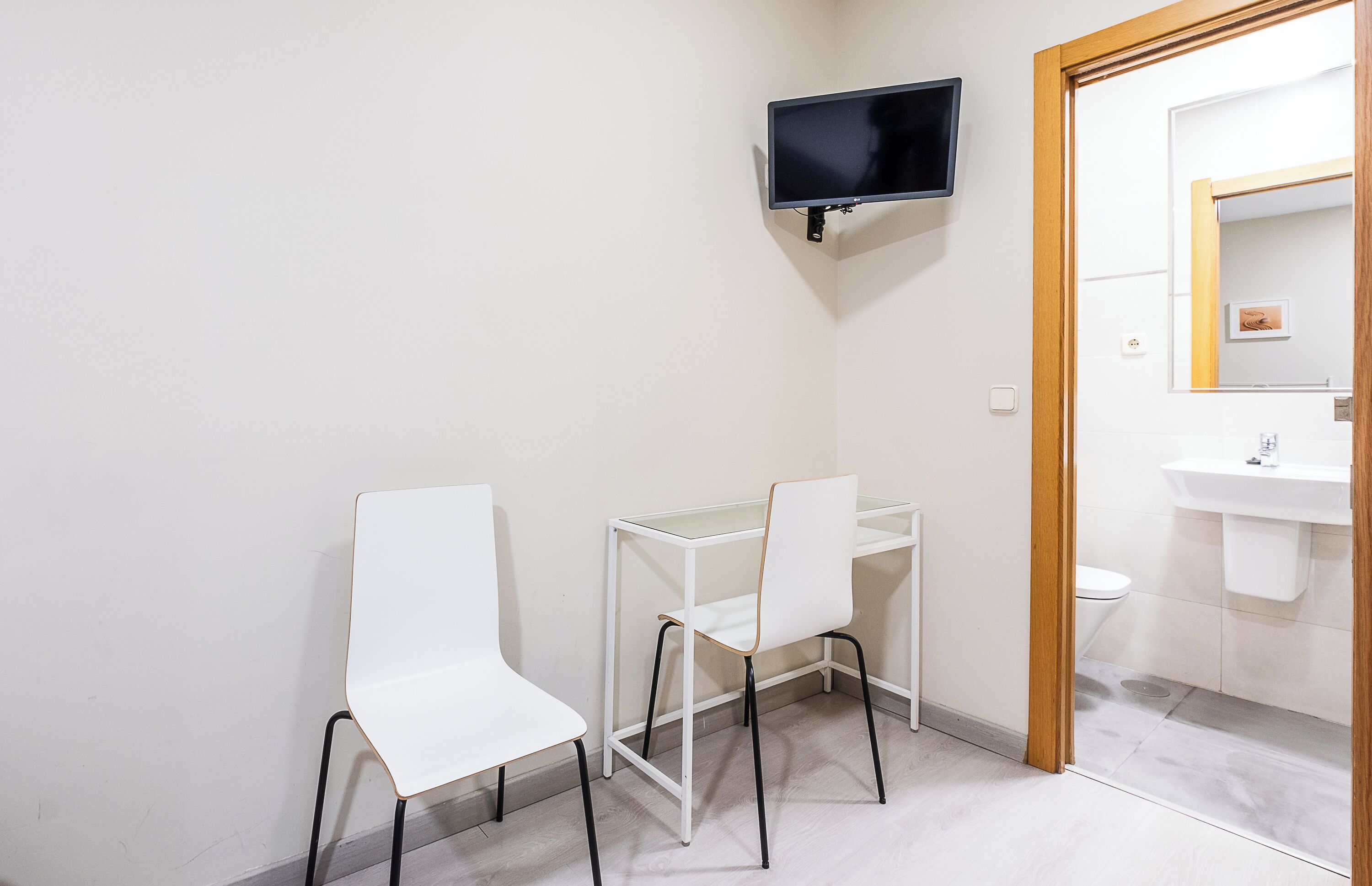 Un baño pequeño y moderno con un tocador blanco, un espejo y un televisor montado en la pared.