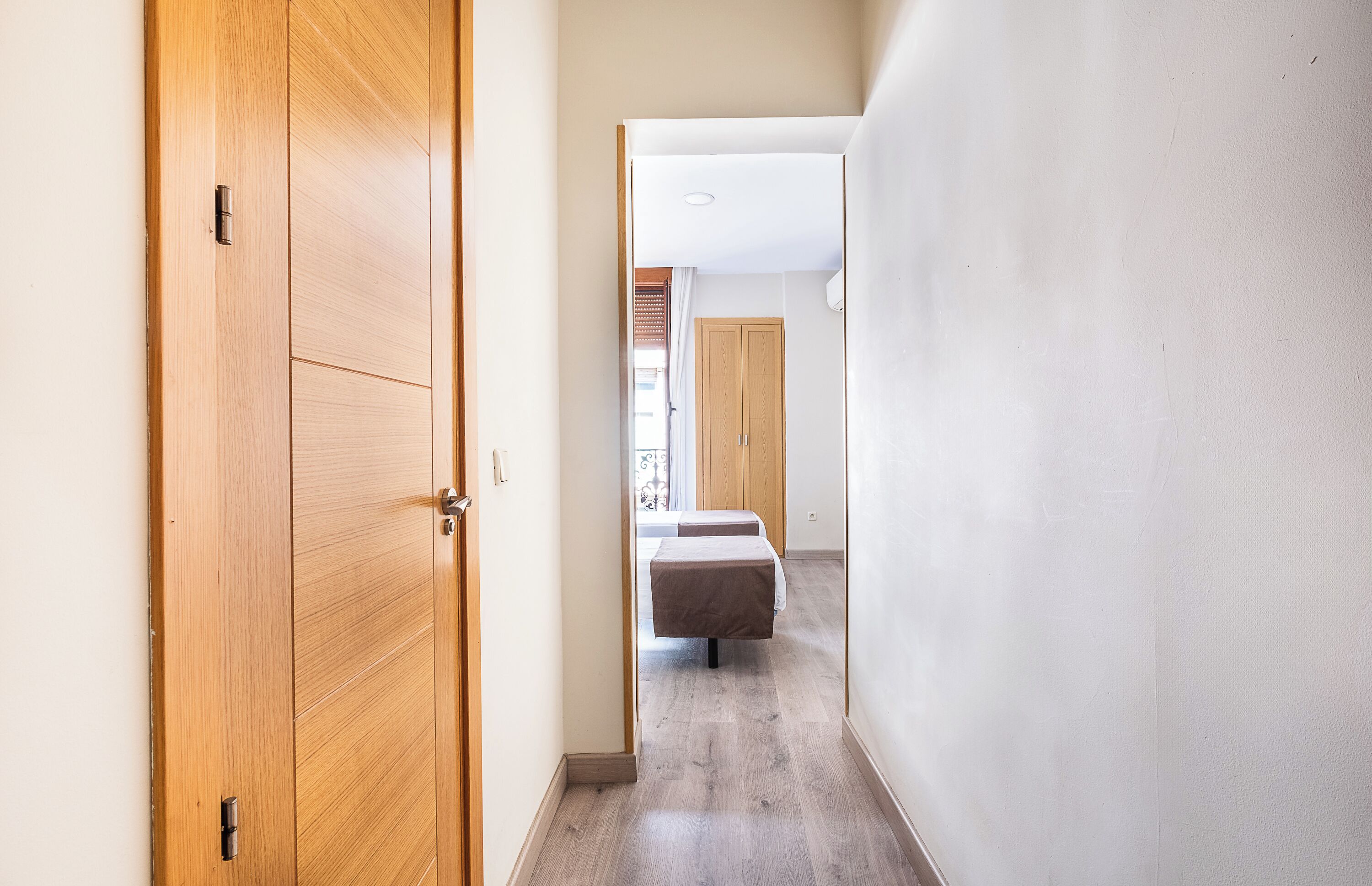 Un pasillo con puerta de madera, cama y armario.