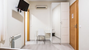 A small, well-lit room with a white desk, a chair, a television mounted on the wall, and a wooden door. - Hostal El Pilar (Madrid)