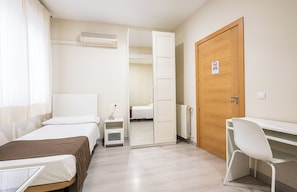 A hotel room with two beds, a desk, a chair, a radiator, and a door with a no-smoking sign. - Hostal El Pilar (Madrid)