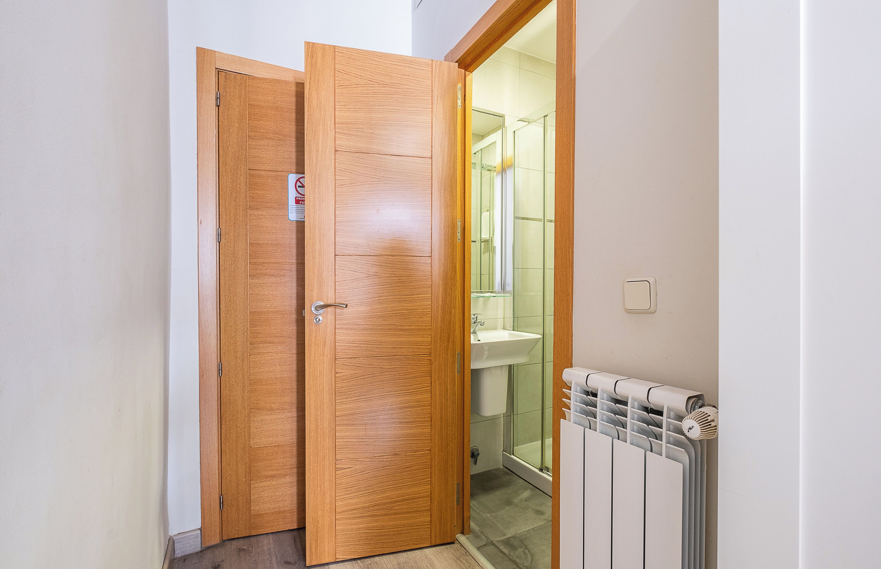 Puerta de madera que da a un baño con cabina de ducha de vidrio y un radiador blanco.