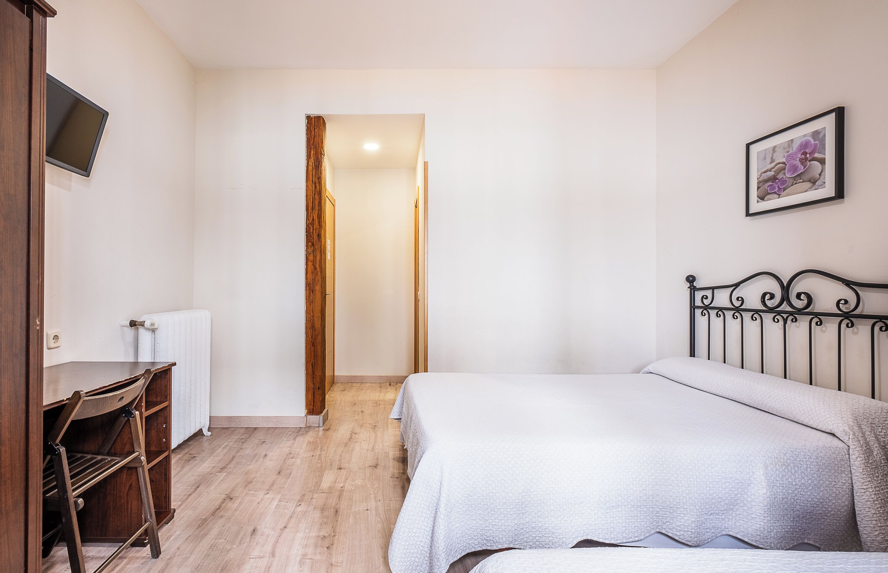 A bedroom with a bed, a desk, a chair, a radiator, and a television.