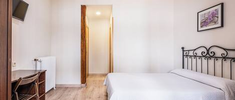 A bedroom with a bed, a desk, a chair, a radiator, and a television.