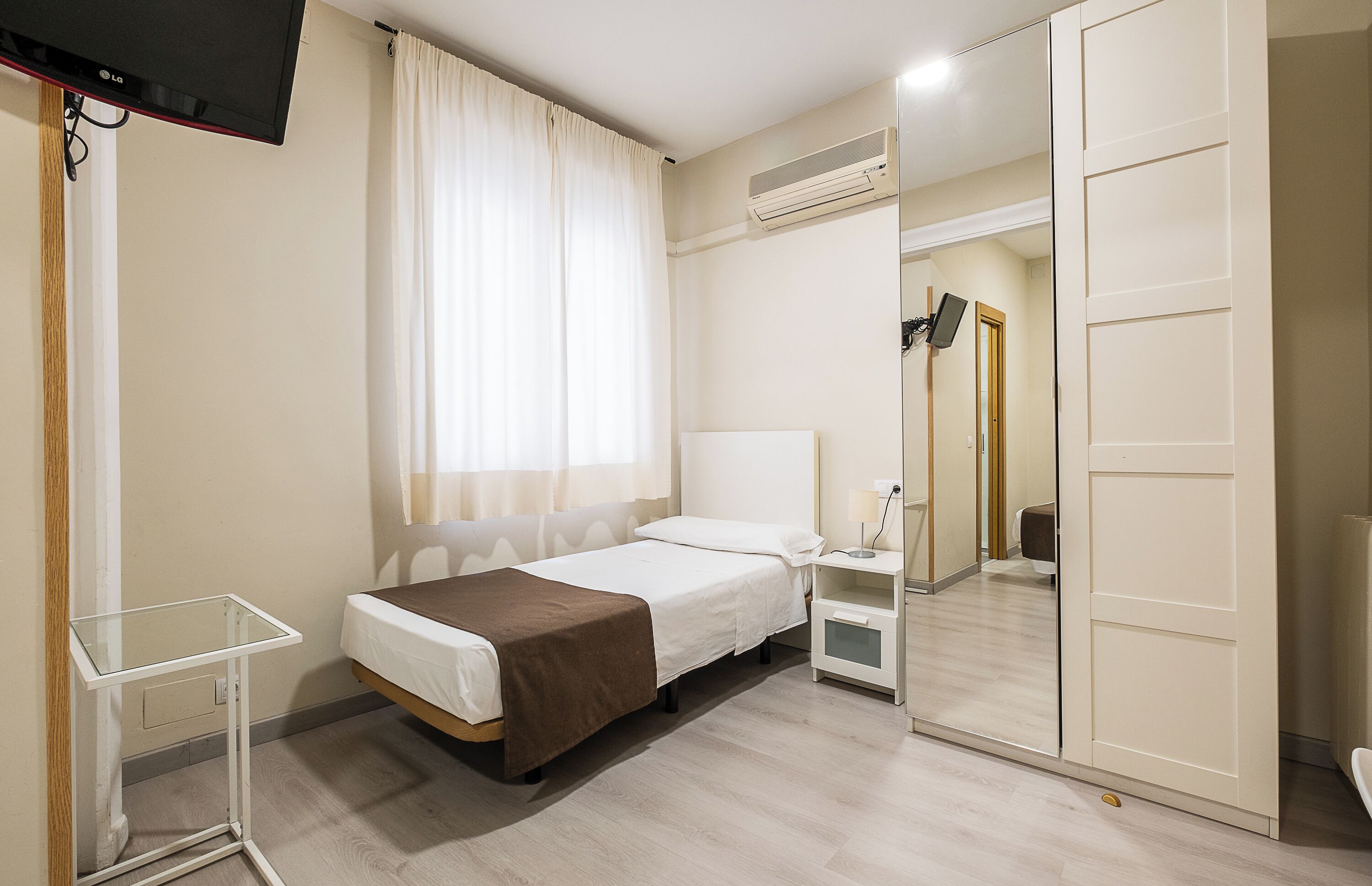 Een hotelkamer met een bed, nachtkastje, lamp, airconditioning en een spiegel.