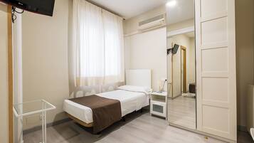 Een hotelkamer met een bed, nachtkastje, lamp, airconditioning en een spiegel.