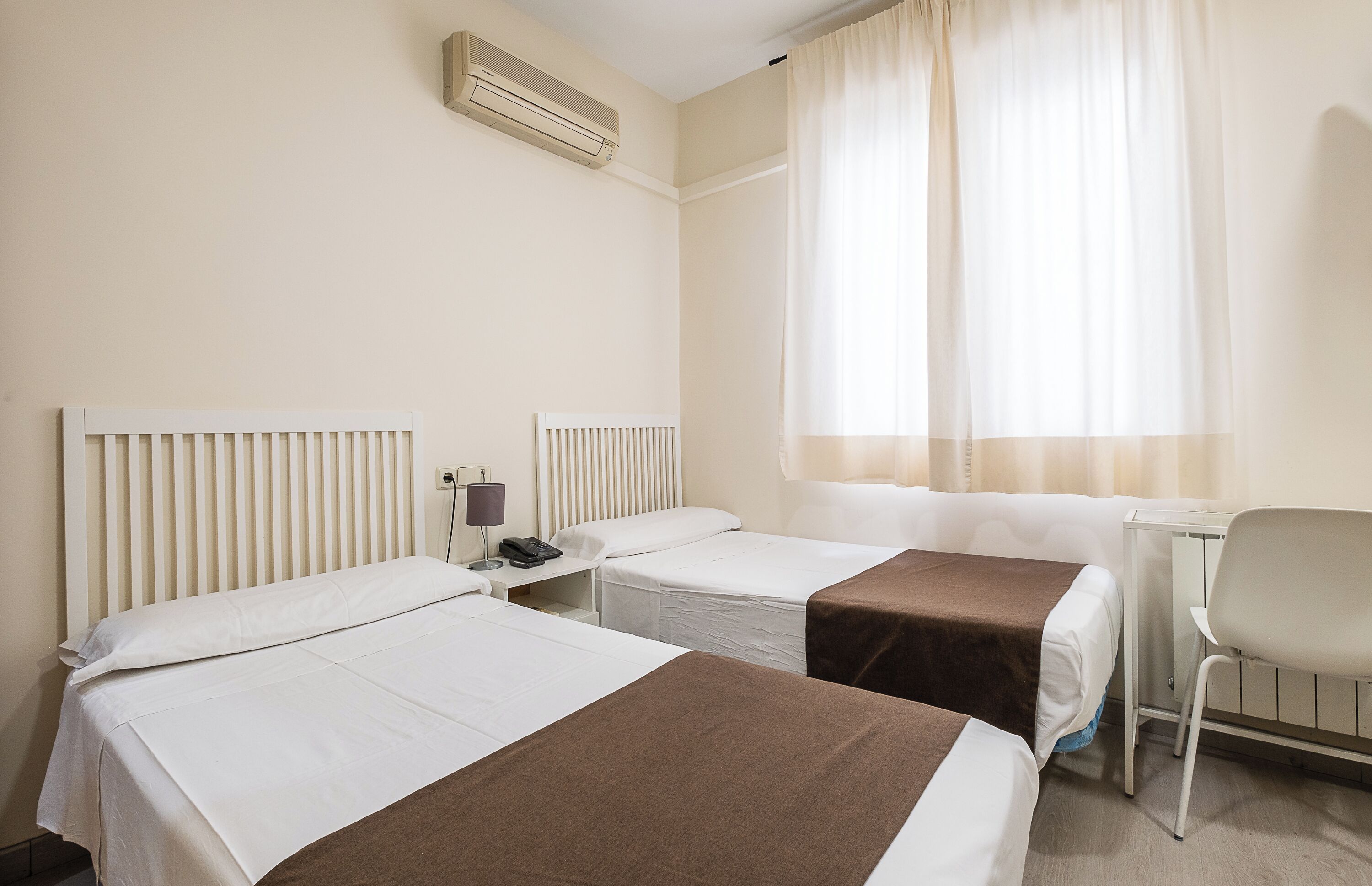A hotel room with two beds, a desk, a chair, and a window with curtains.