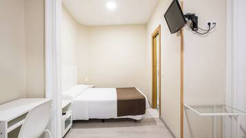 Habitación de hotel con cama, escritorio, silla, televisor montado en la pared y una mesita.