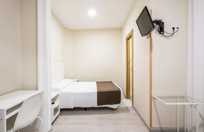 A hotel room with a bed, a desk, a chair, a TV mounted on the wall, and a small table. - Hostal El Pilar (Madrid)