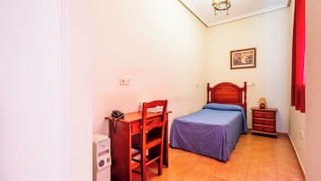 Een kleine slaapkamer met een enkel bed, een nachtkastje, een bureau met stoel, een telefoon aan de muur en een plafondlamp.
